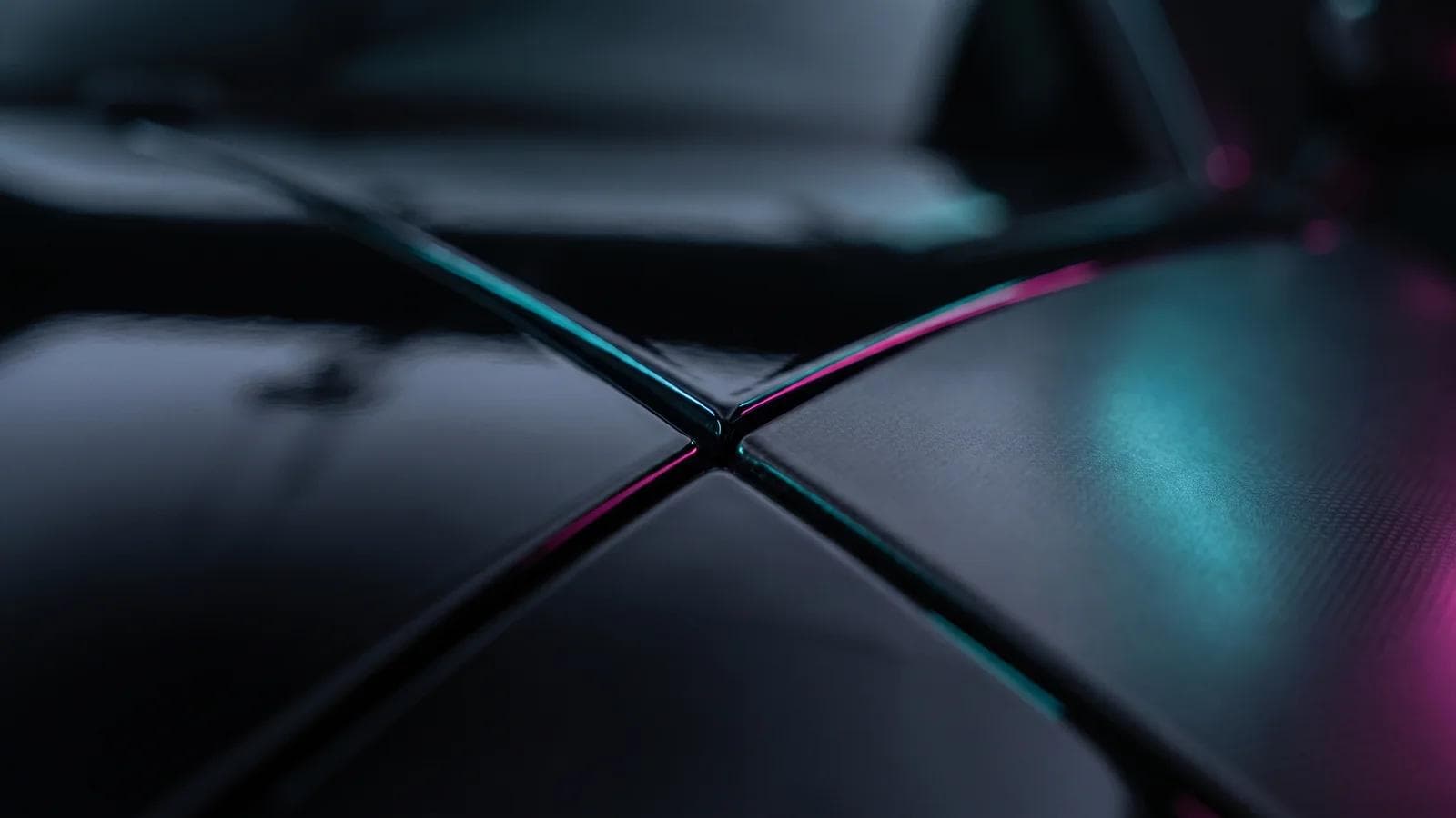 Drei glänzende schwarze Lackflächen nebeneinander: spiegelnde Keramikversiegelung, hauchdünne PPF-Folienkante und satinierte Farbfolie in türkis-magentafarbenem Neonlicht.